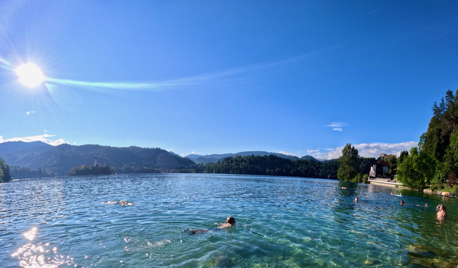 People swimming in a lake with mountains and a church in the background.
